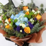 Floral Forest Bouquet: Blue Hydrangea, Orange Roses, White Baby Roses, Eryngium, Green Button Chrysanthemum, Blue Statice | Brown and Black Wrap