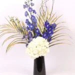 Heavenly Blooms: Flowers Artfully Arranged in Black Vase ? White Hydrangea, Blue Delphinium, Golden Sprayed Areca Palm Leaves